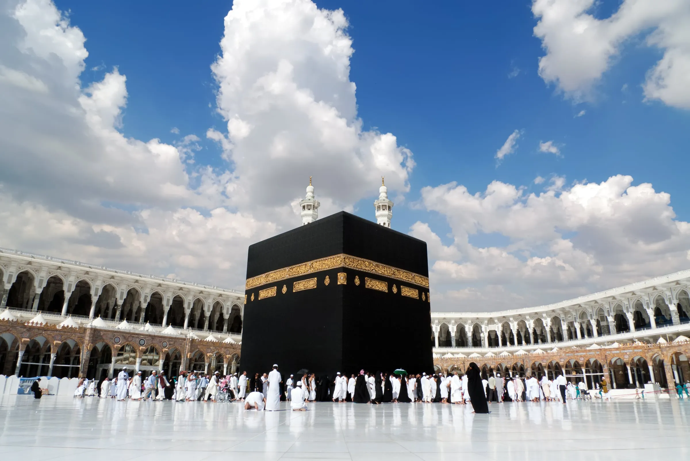 Pilgrims in ihram around the Kaaba under a blue sky